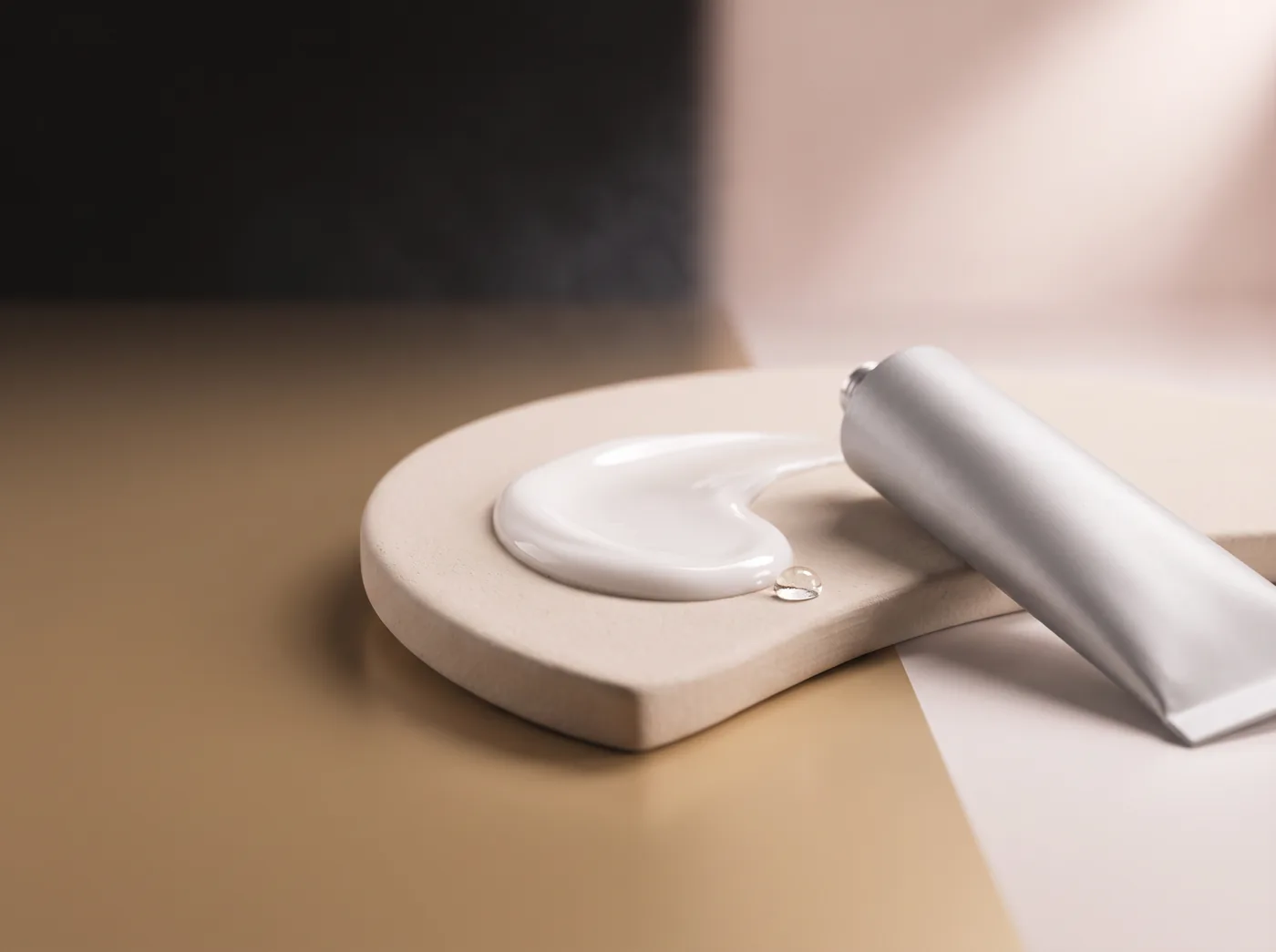 Volute de crème blanche sur une plaque de céramique, à côté d'un tube en aluminium non marqué